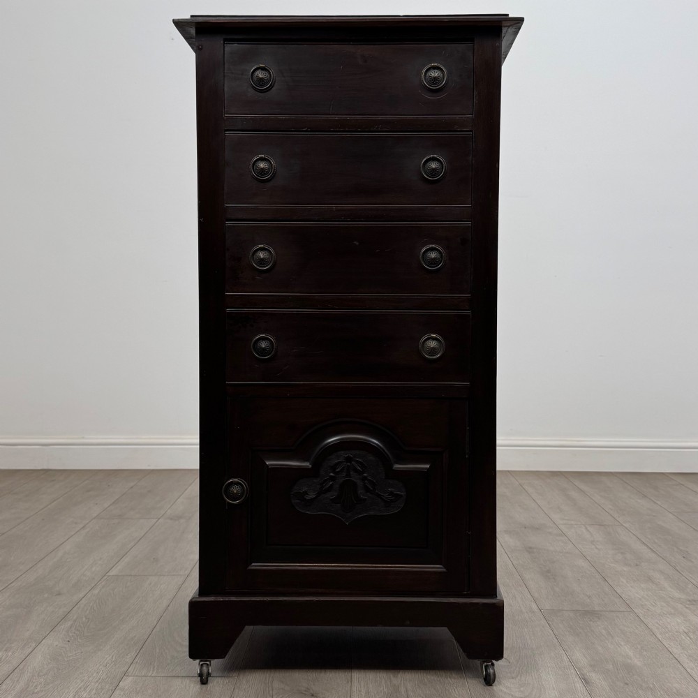 A tall, dark mahogany Edwardian chest features four stacked drawers above a single carved cupboard door, set on small brass castors.