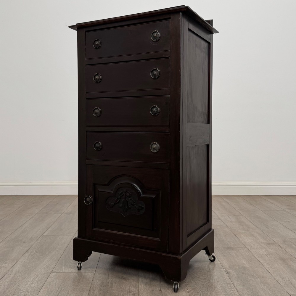 A tall, dark mahogany Edwardian chest features four stacked drawers above a single carved cupboard door, set on small brass castors. View III