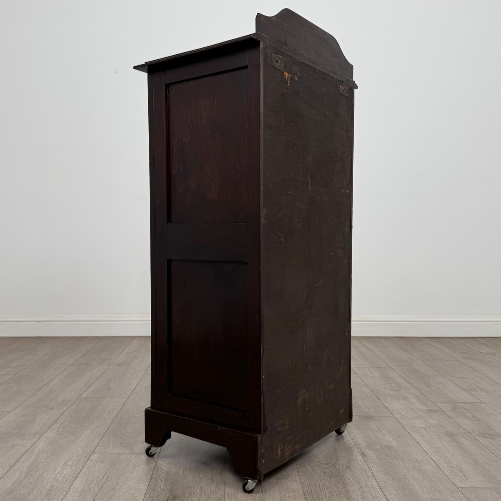 A tall, dark mahogany Edwardian chest features four stacked drawers above a single carved cupboard door, set on small brass castors. View V