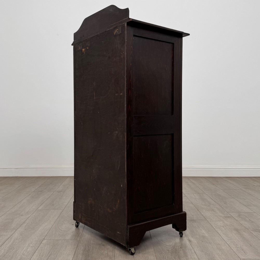 A tall, dark mahogany Edwardian chest features four stacked drawers above a single carved cupboard door, set on small brass castors. View VII
