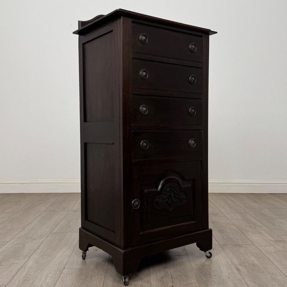 A tall, dark mahogany Edwardian chest features four stacked drawers above a single carved cupboard door, set on small brass castors. View IX