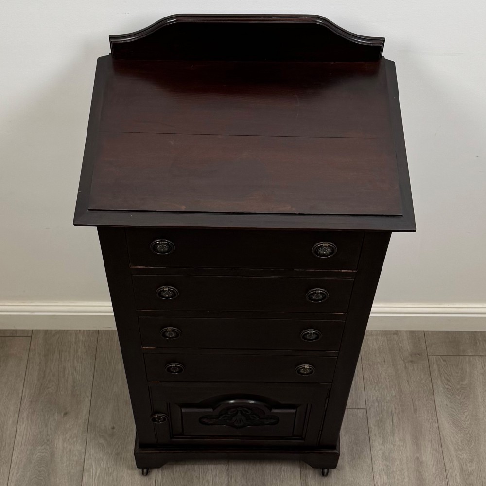 A tall, dark mahogany Edwardian chest features four stacked drawers above a single carved cupboard door, set on small brass castors. View X