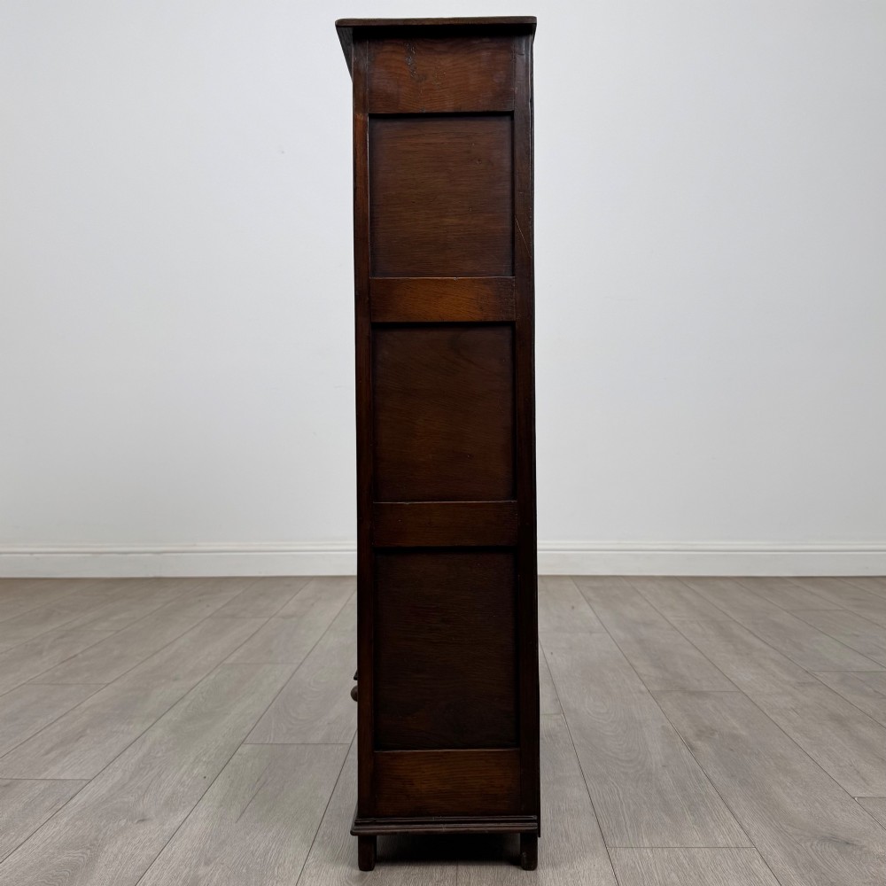 A dark oak open bookcase featuring a carved top frieze, three open display shelves, and a single bottom drawer with a central wooden knob handle. View IV