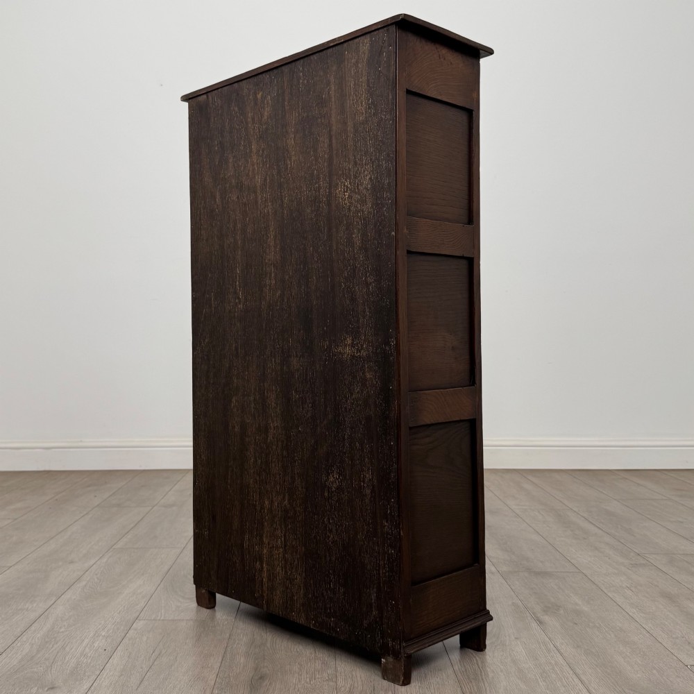 A dark oak open bookcase featuring a carved top frieze, three open display shelves, and a single bottom drawer with a central wooden knob handle. View VII