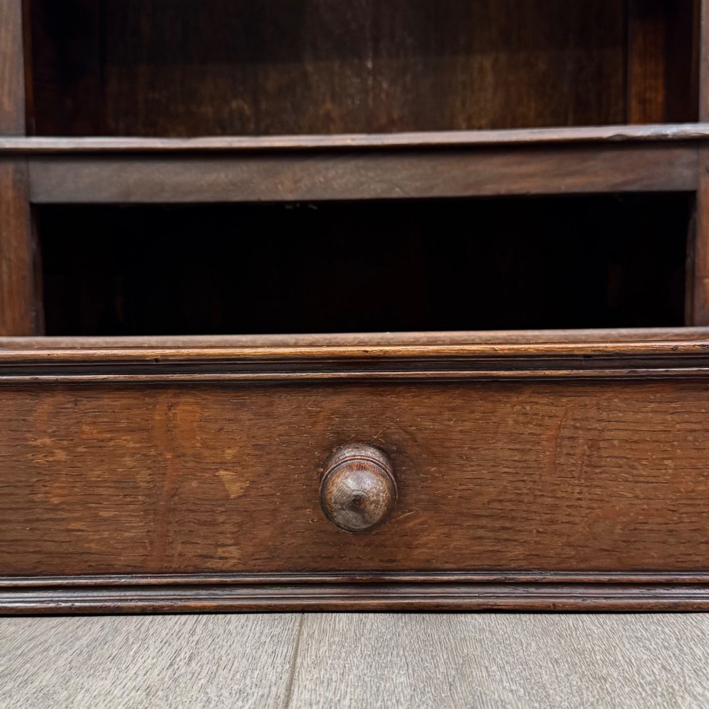 A dark oak open bookcase featuring a carved top frieze, three open display shelves, and a single bottom drawer with a central wooden knob handle. View XII