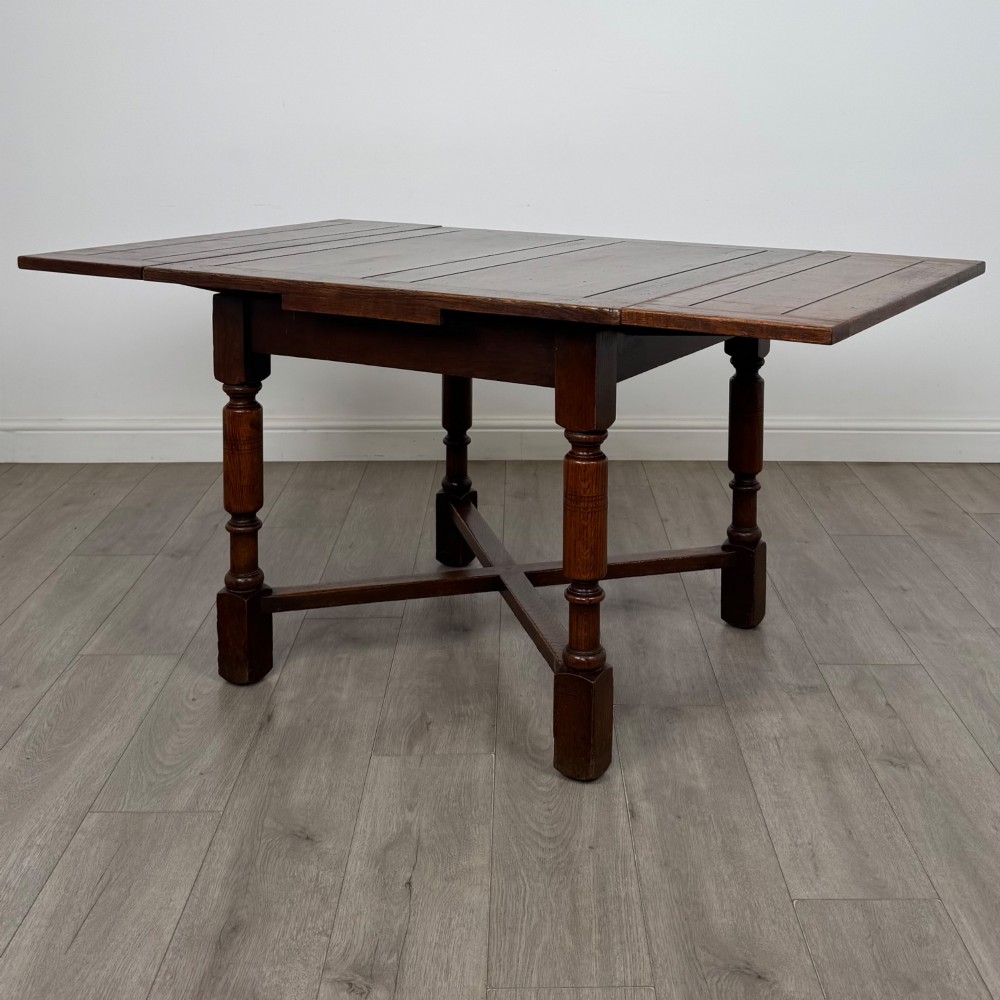 An Edwardian oak draw-leaf dining table featuring turned legs, a rectangular plank top, and an X-shaped cross stretcher base.
