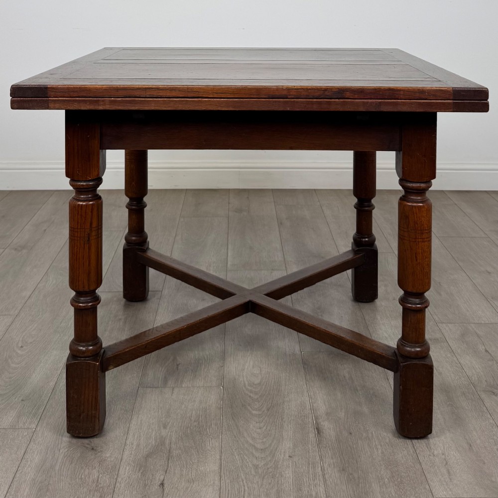 An Edwardian oak draw-leaf dining table featuring turned legs, a rectangular plank top, and an X-shaped cross stretcher base. View IV