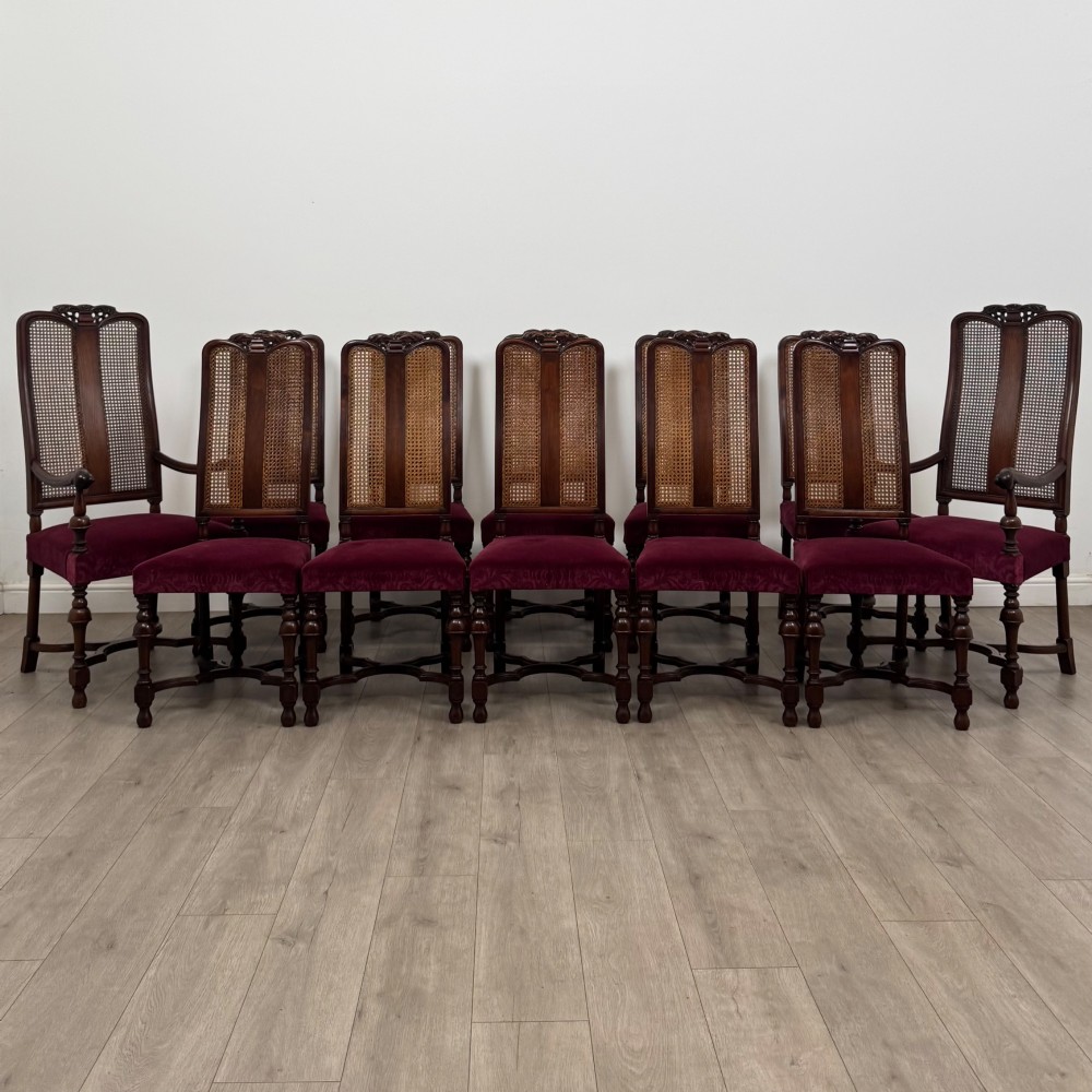 A set of twelve mahogany dining chairs featuring high cane-back panels, carved cresting rails, turned legs, and deep red velvet upholstered seats.