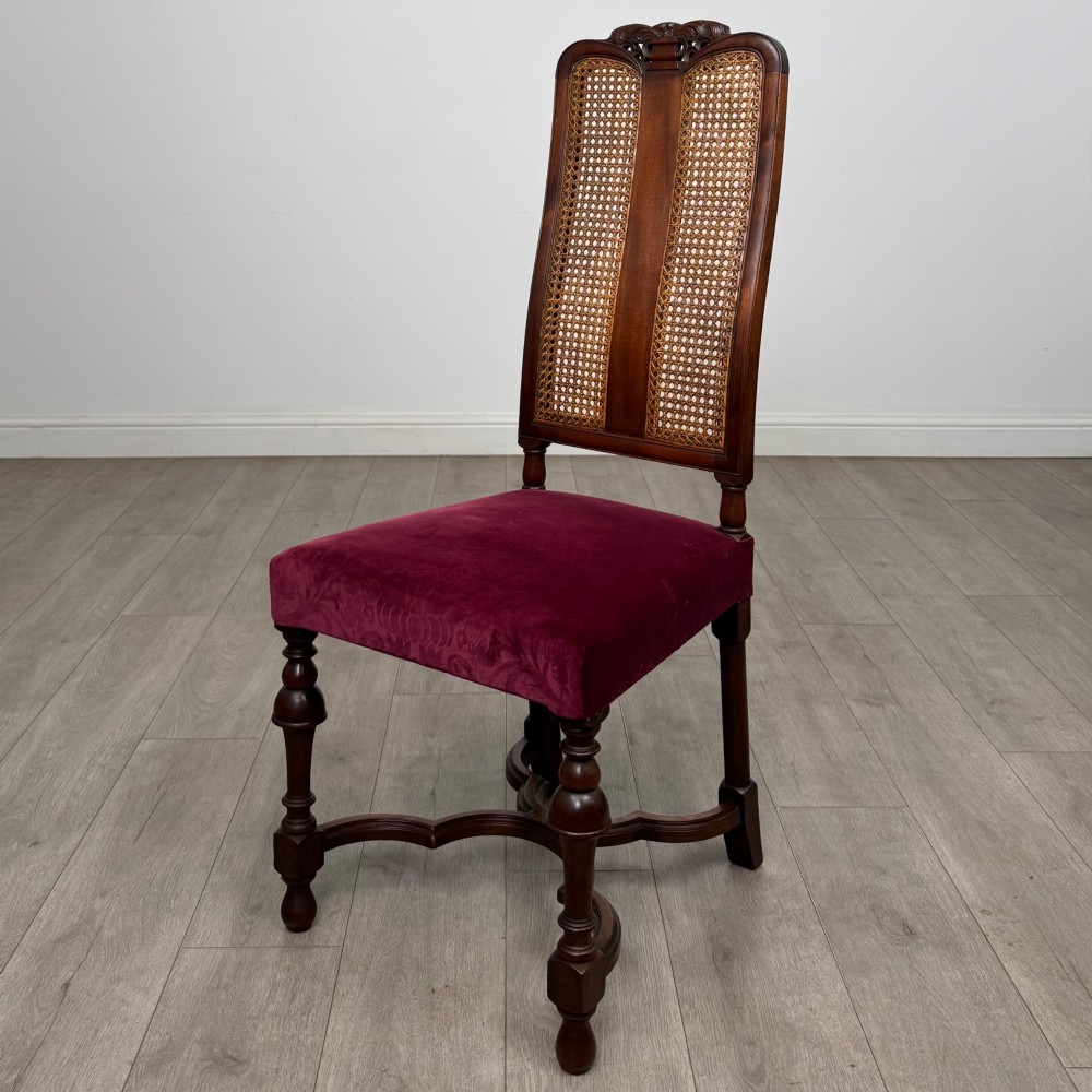 A set of twelve mahogany dining chairs featuring high cane-back panels, carved cresting rails, turned legs, and deep red velvet upholstered seats. View III