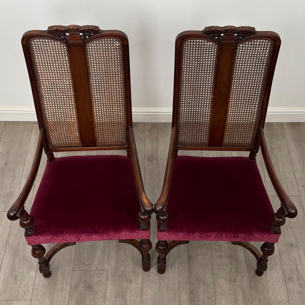 A set of twelve mahogany dining chairs featuring high cane-back panels, carved cresting rails, turned legs, and deep red velvet upholstered seats. View X