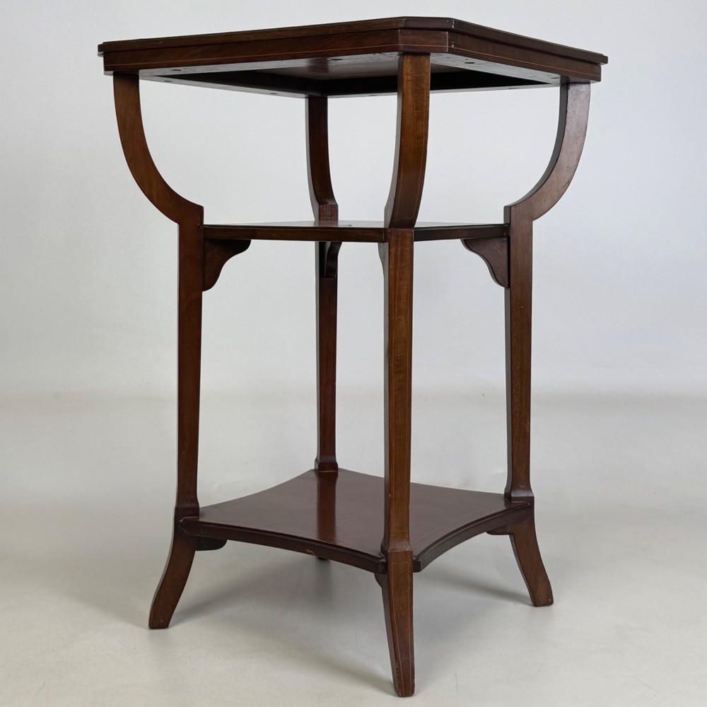 An Edwardian dark mahogany side table featuring a square top, sweeping curved leg supports, and two lower shelves.