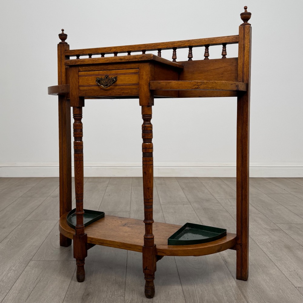 An Edwardian golden oak hall stand with a top spindle gallery, central glove drawer with brass handle, twin umbrella rail apertures, and metal drip trays on the lower shelf. View II