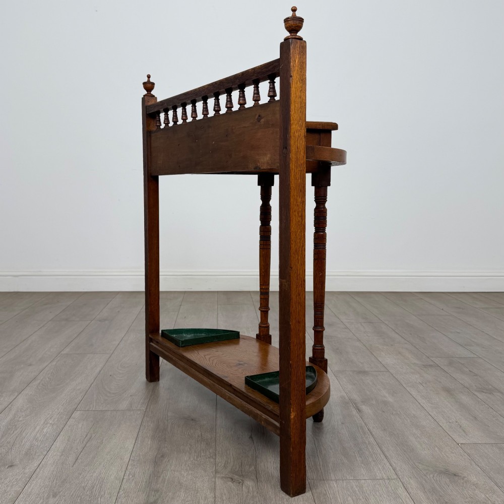 An Edwardian golden oak hall stand with a top spindle gallery, central glove drawer with brass handle, twin umbrella rail apertures, and metal drip trays on the lower shelf. View VI