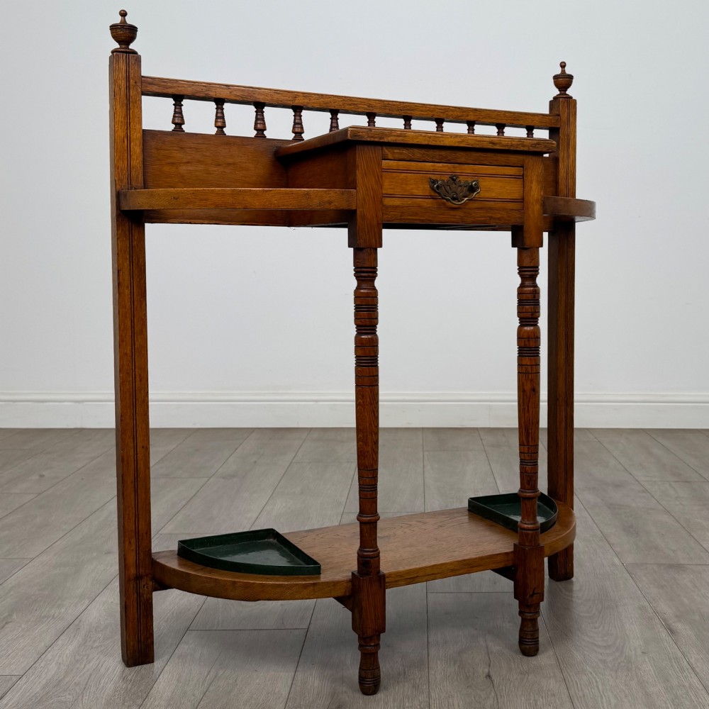 An Edwardian golden oak hall stand with a top spindle gallery, central glove drawer with brass handle, twin umbrella rail apertures, and metal drip trays on the lower shelf. View VIII