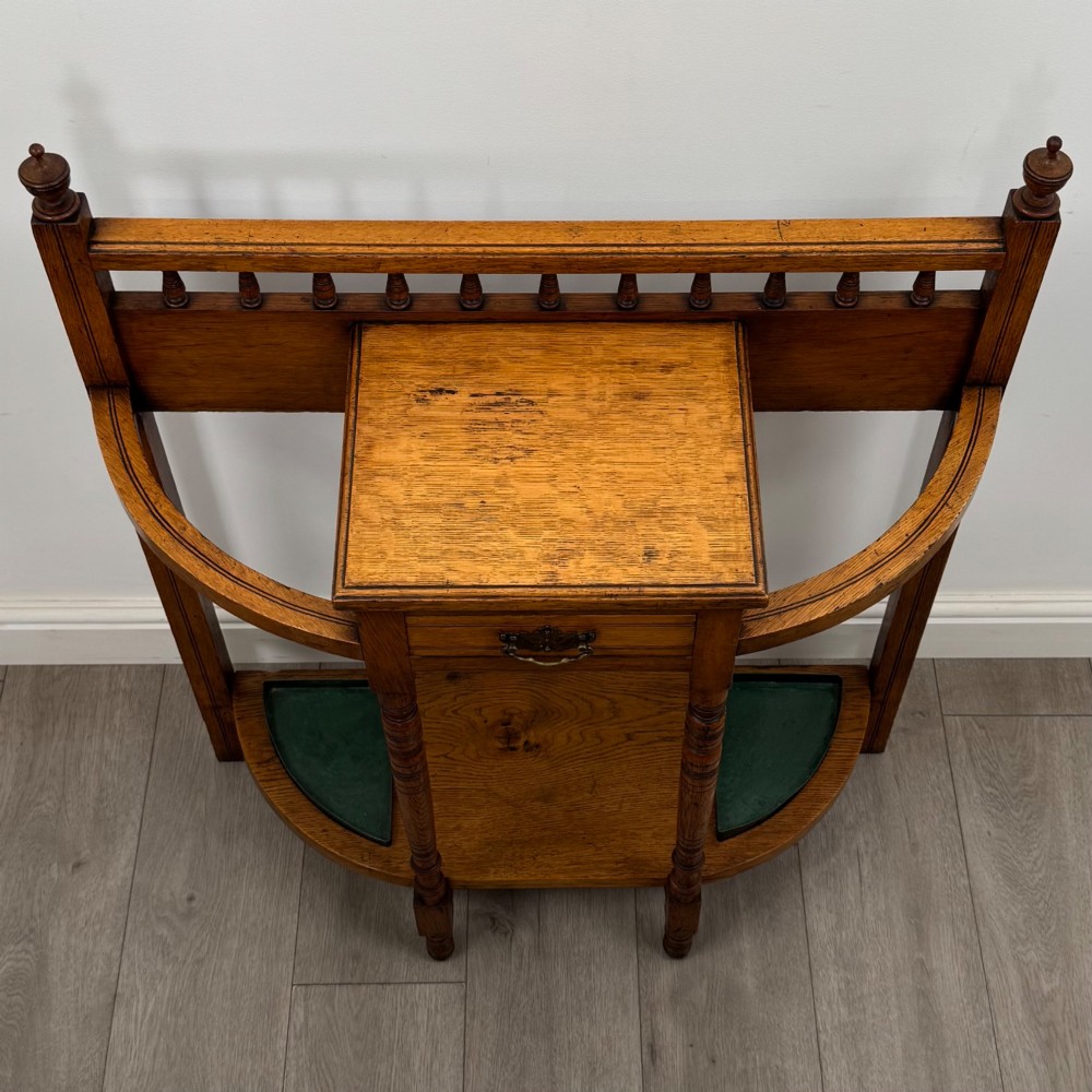 An Edwardian golden oak hall stand with a top spindle gallery, central glove drawer with brass handle, twin umbrella rail apertures, and metal drip trays on the lower shelf. View IX