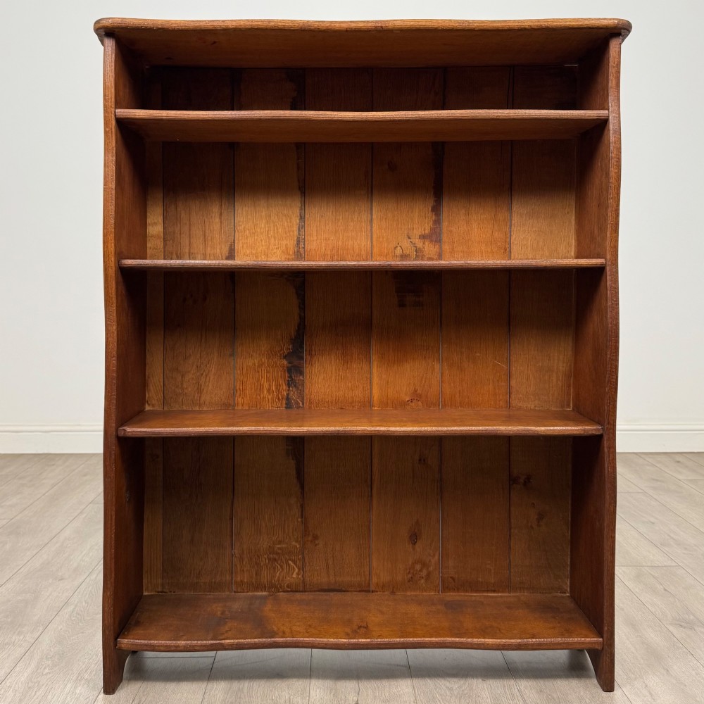 An early 20th-century medium brown solid oak open bookcase featuring four fixed shelves and a planked back panel.