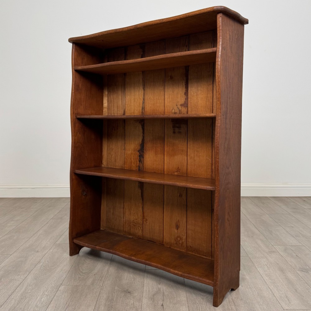 An early 20th-century medium brown solid oak open bookcase featuring four fixed shelves and a planked back panel. View II