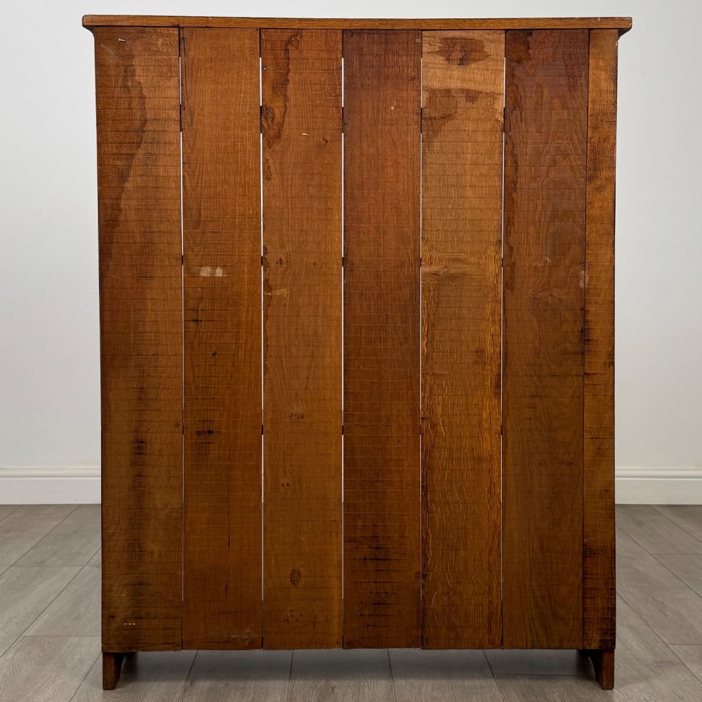An early 20th-century medium brown solid oak open bookcase featuring four fixed shelves and a planked back panel. View V