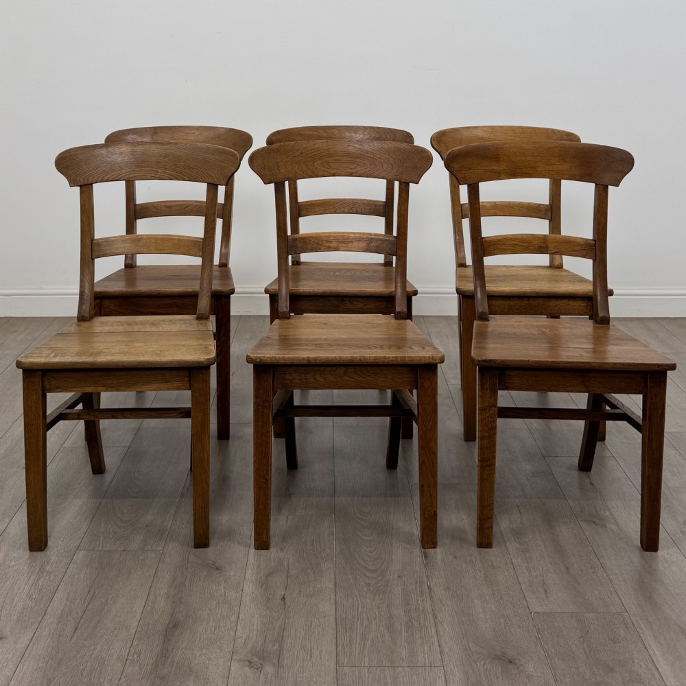 A set of six Victorian solid oak dining chairs featuring curved backrails, solid wooden seats, and square legs with stretchers.