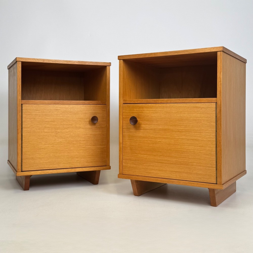 A pair of mid-century modern warm brown teak bedside cabinets featuring open upper shelf cubbies, lower cupboard doors with dark round wooden knobs, and low angled feet.