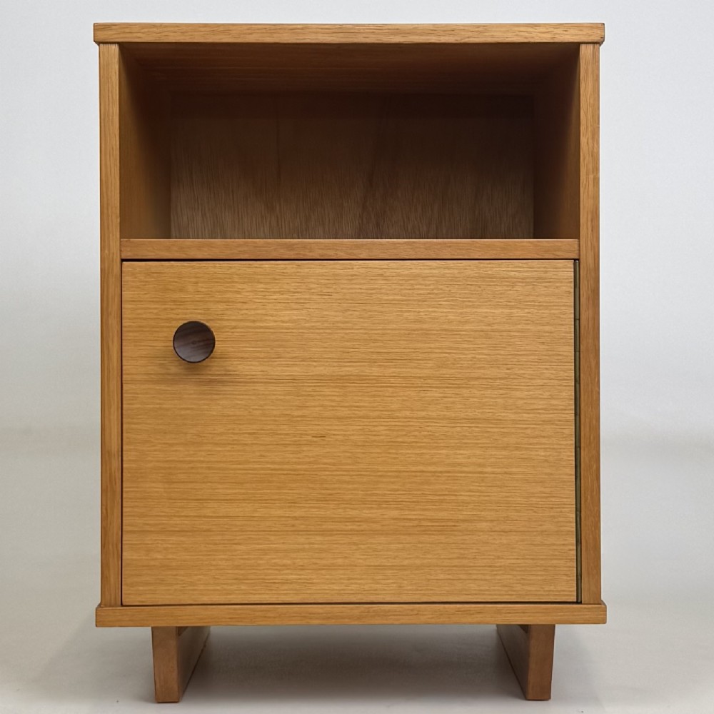 A pair of mid-century modern warm brown teak bedside cabinets featuring open upper shelf cubbies, lower cupboard doors with dark round wooden knobs, and low angled feet. View II