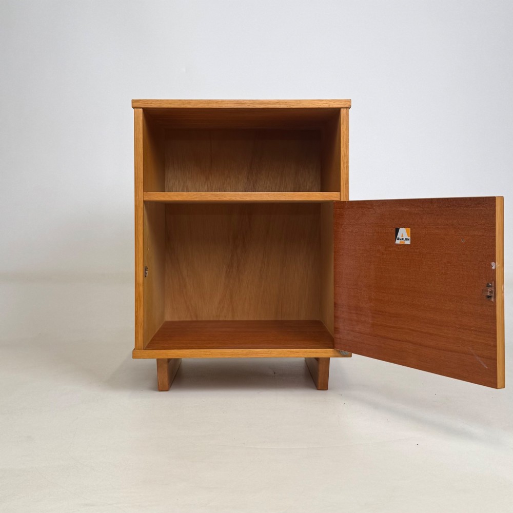 A pair of mid-century modern warm brown teak bedside cabinets featuring open upper shelf cubbies, lower cupboard doors with dark round wooden knobs, and low angled feet. View III