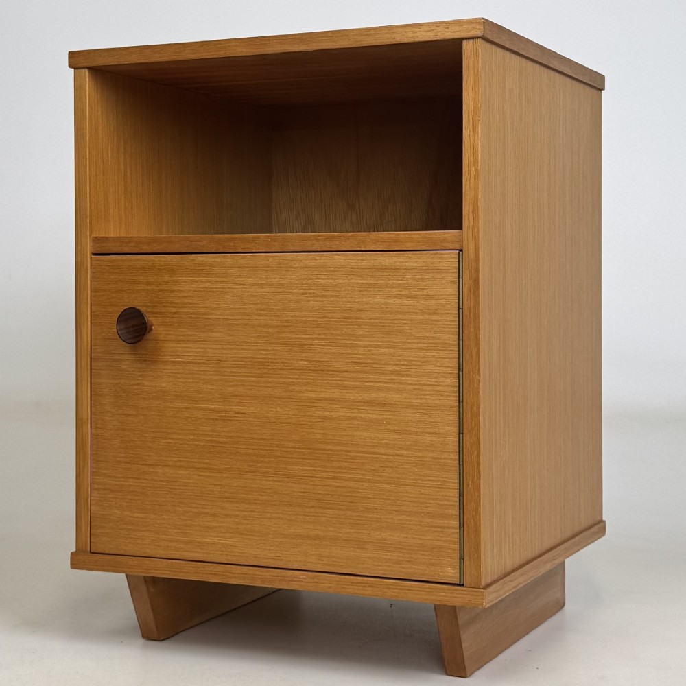 A pair of mid-century modern warm brown teak bedside cabinets featuring open upper shelf cubbies, lower cupboard doors with dark round wooden knobs, and low angled feet. View IV