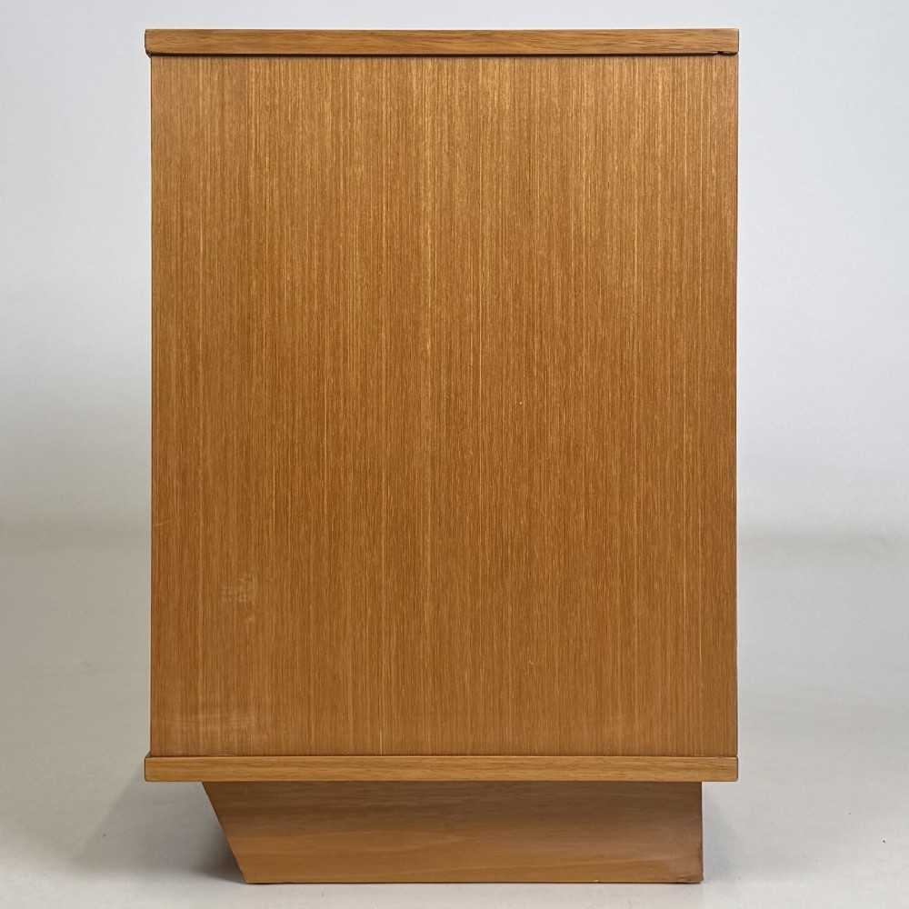 A pair of mid-century modern warm brown teak bedside cabinets featuring open upper shelf cubbies, lower cupboard doors with dark round wooden knobs, and low angled feet. View V