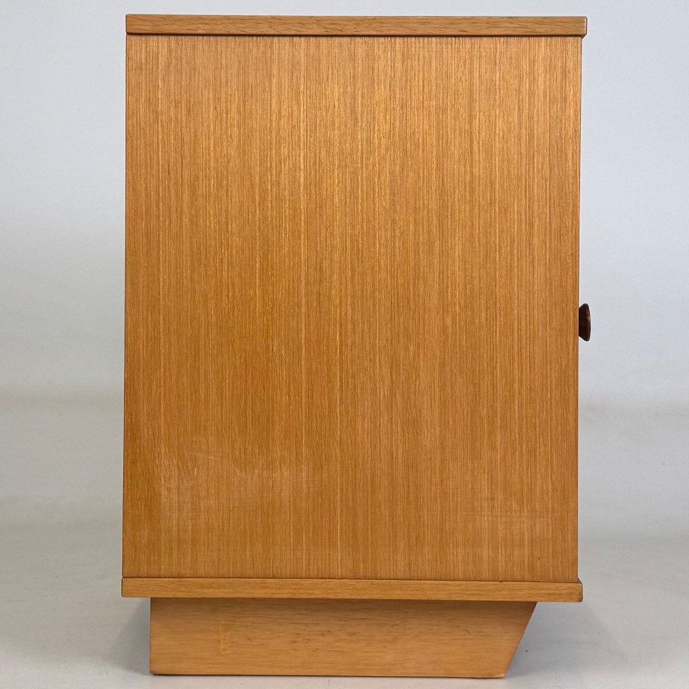 A pair of mid-century modern warm brown teak bedside cabinets featuring open upper shelf cubbies, lower cupboard doors with dark round wooden knobs, and low angled feet. View IX