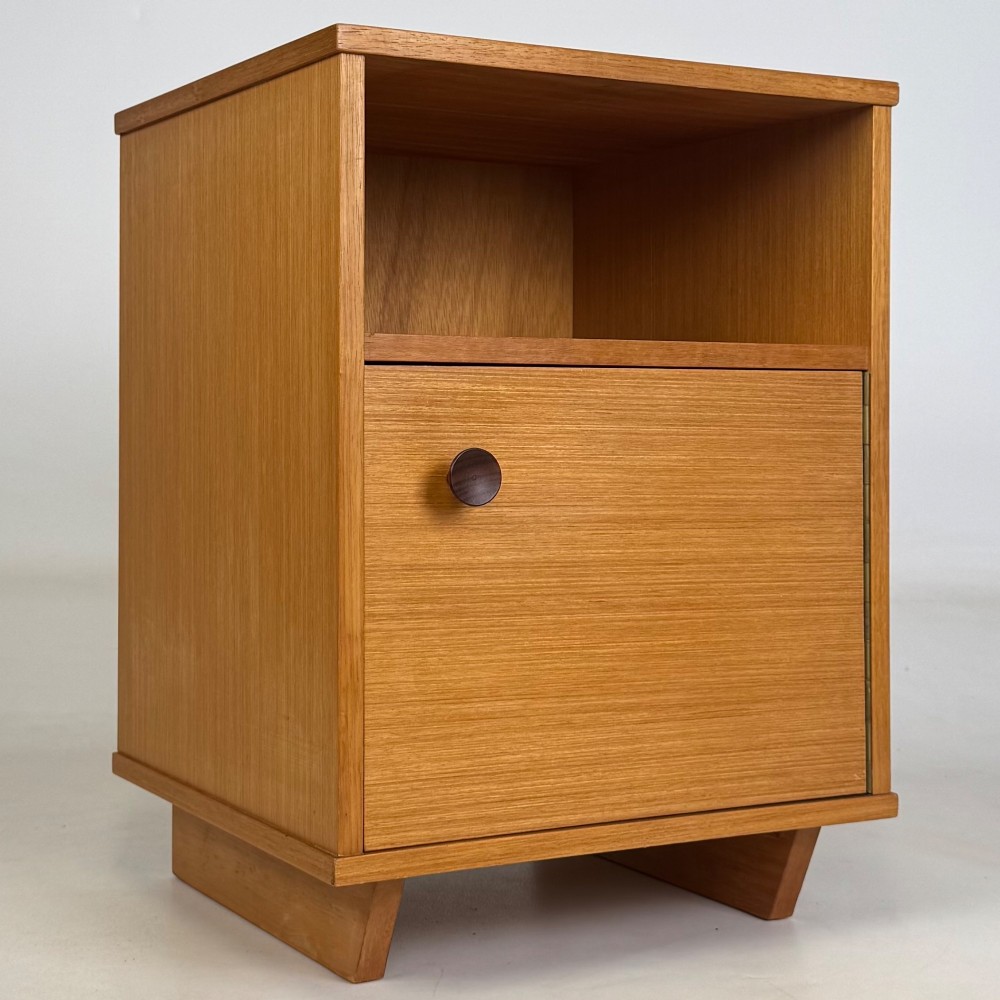 A pair of mid-century modern warm brown teak bedside cabinets featuring open upper shelf cubbies, lower cupboard doors with dark round wooden knobs, and low angled feet. View X