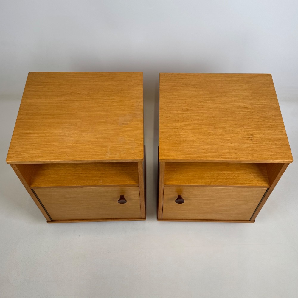 A pair of mid-century modern warm brown teak bedside cabinets featuring open upper shelf cubbies, lower cupboard doors with dark round wooden knobs, and low angled feet. View XI