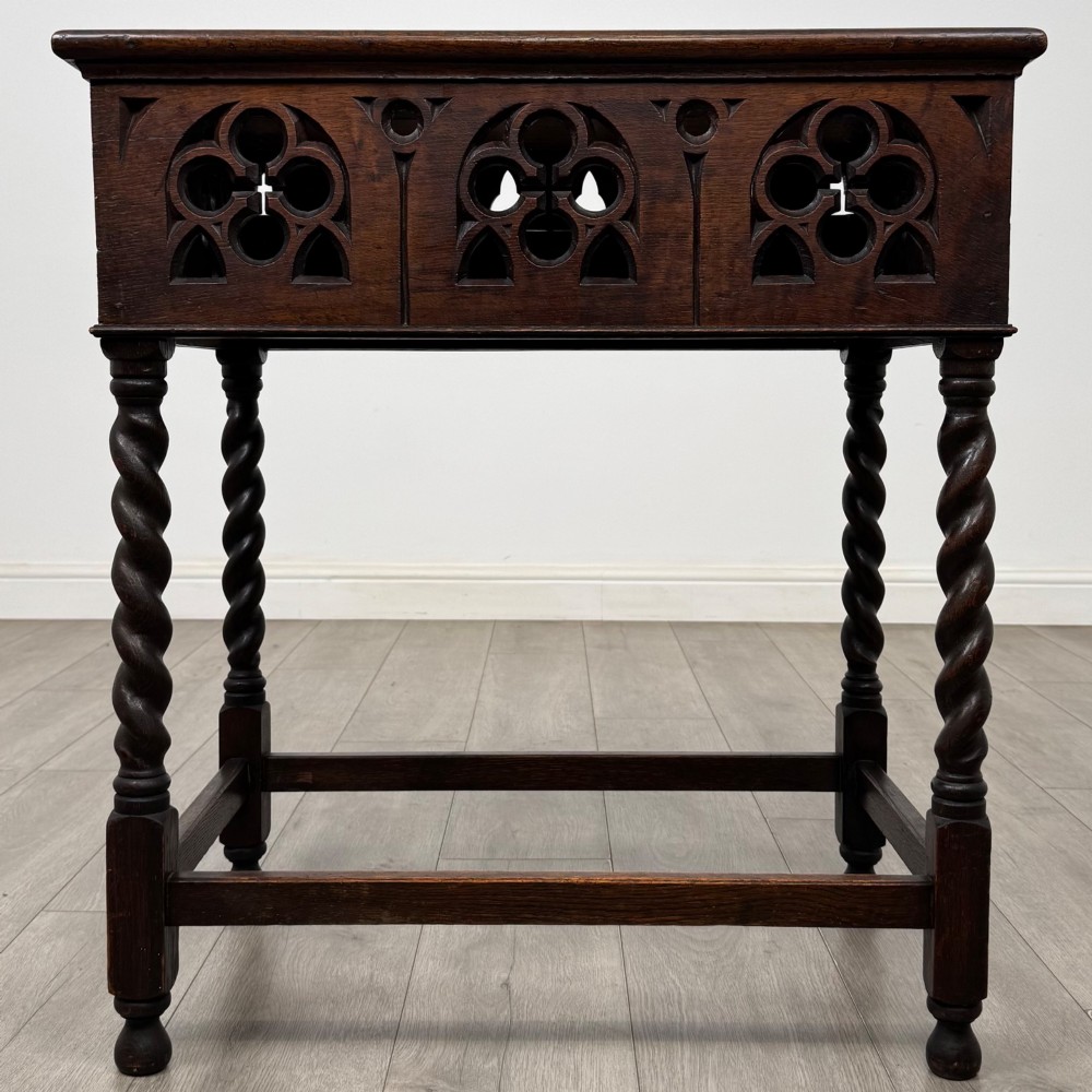 A dark oak Gothic style side table featuring three pierced tracery carved panels on the apron and four barley twist legs connected by box stretchers.
