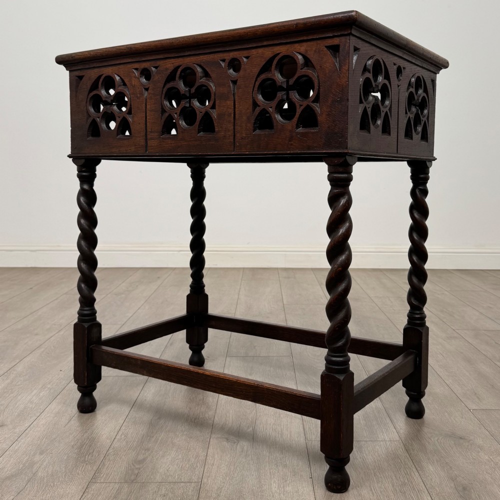 A dark oak Gothic style side table featuring three pierced tracery carved panels on the apron and four barley twist legs connected by box stretchers. View II