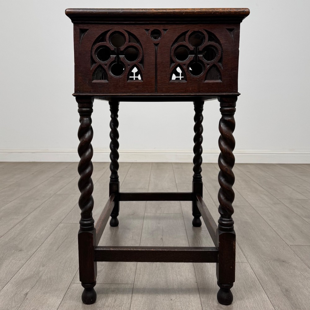 A dark oak Gothic style side table featuring three pierced tracery carved panels on the apron and four barley twist legs connected by box stretchers. View III