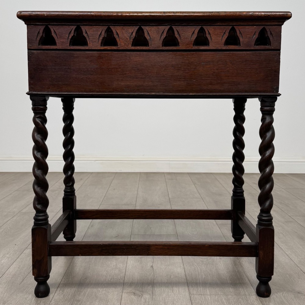 A dark oak Gothic style side table featuring three pierced tracery carved panels on the apron and four barley twist legs connected by box stretchers. View V