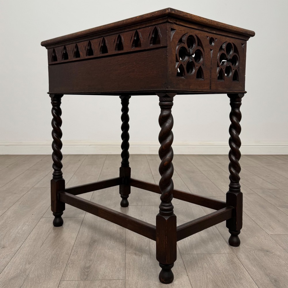 A dark oak Gothic style side table featuring three pierced tracery carved panels on the apron and four barley twist legs connected by box stretchers. View VI