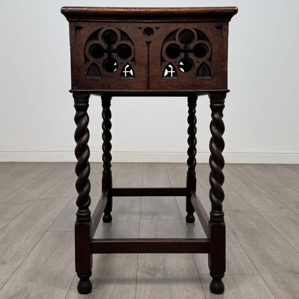 A dark oak Gothic style side table featuring three pierced tracery carved panels on the apron and four barley twist legs connected by box stretchers. View VII