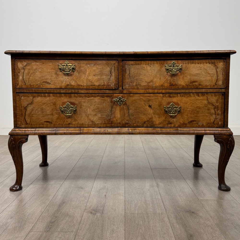 An 18th-century Queen Anne walnut chest of drawers featuring figured wood veneer, brass drop handles, and cabriole legs ending in pad feet.