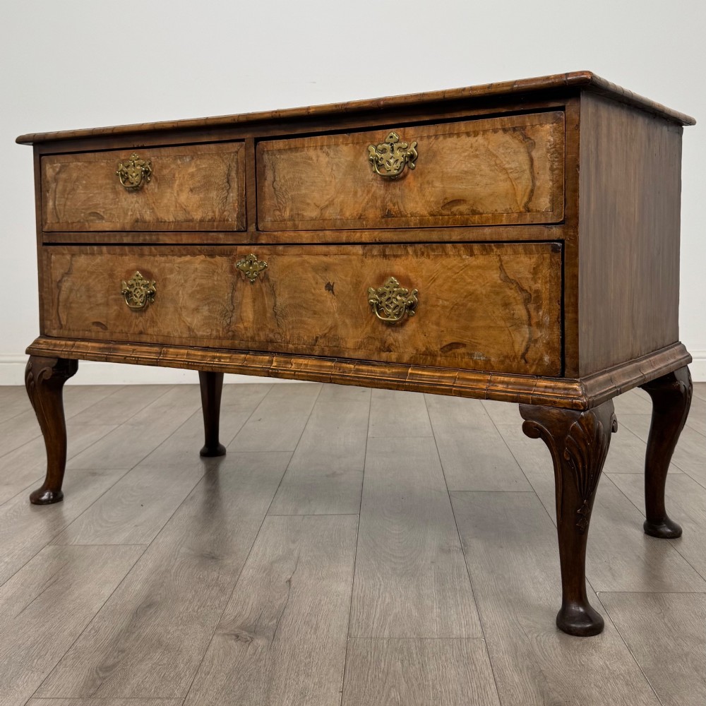 An 18th-century Queen Anne walnut chest of drawers featuring figured wood veneer, brass drop handles, and cabriole legs ending in pad feet. View II