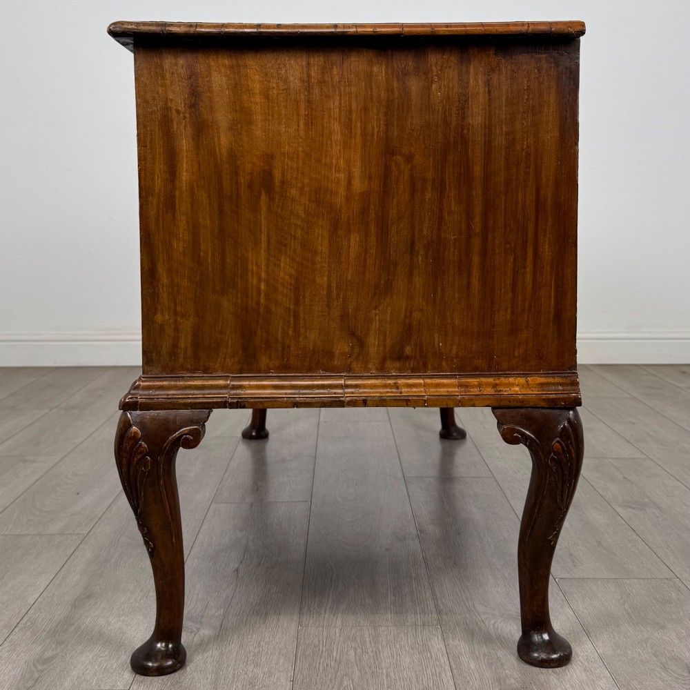 An 18th-century Queen Anne walnut chest of drawers featuring figured wood veneer, brass drop handles, and cabriole legs ending in pad feet. View III