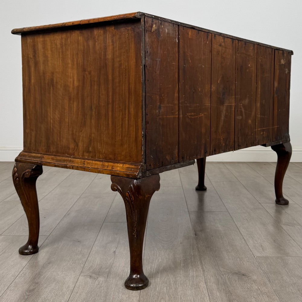 An 18th-century Queen Anne walnut chest of drawers featuring figured wood veneer, brass drop handles, and cabriole legs ending in pad feet. View IV