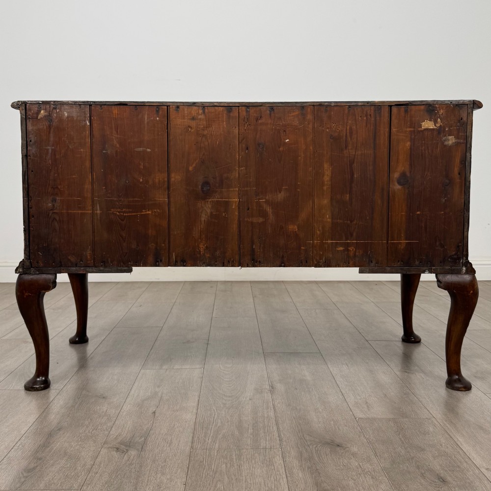 An 18th-century Queen Anne walnut chest of drawers featuring figured wood veneer, brass drop handles, and cabriole legs ending in pad feet. View V