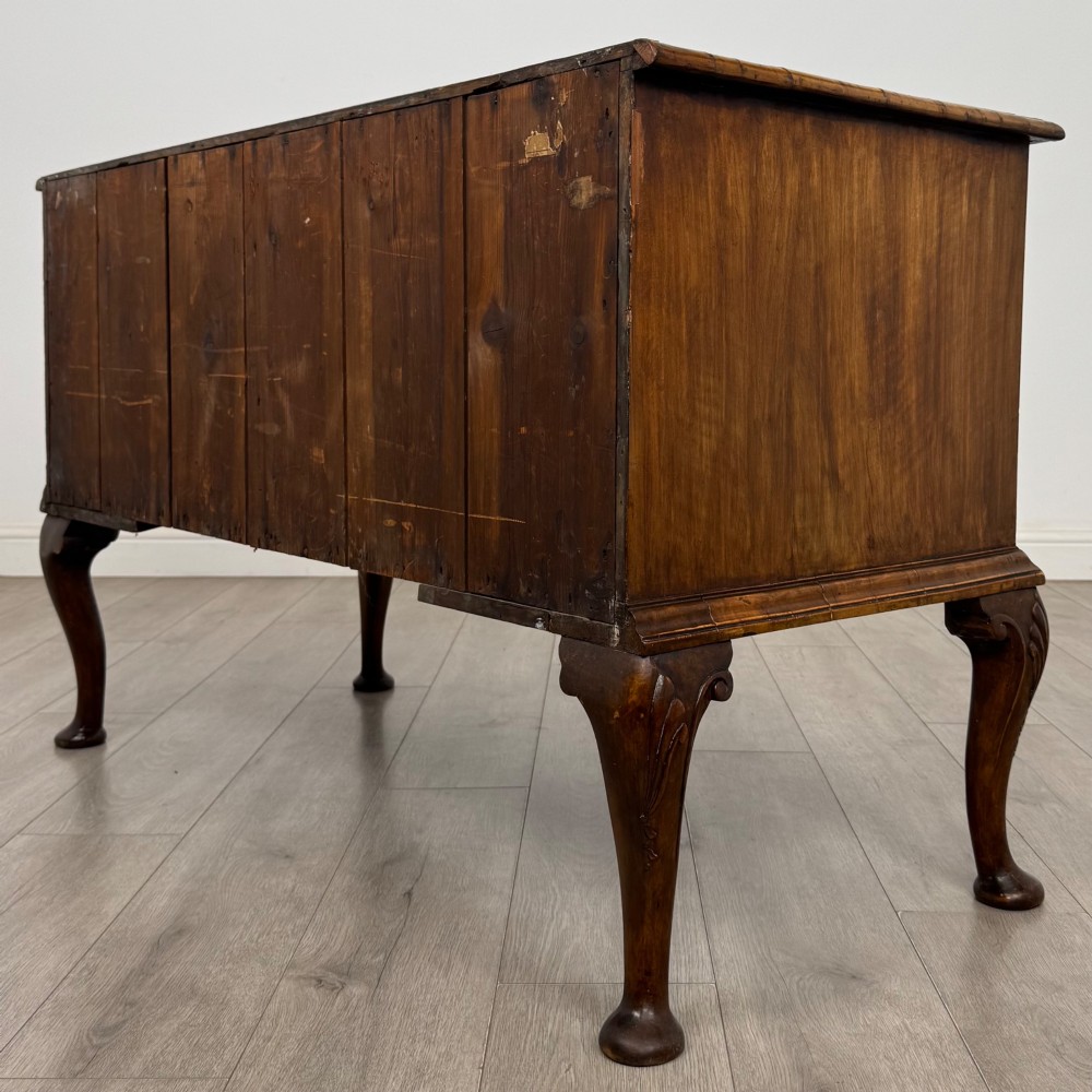An 18th-century Queen Anne walnut chest of drawers featuring figured wood veneer, brass drop handles, and cabriole legs ending in pad feet. View VI