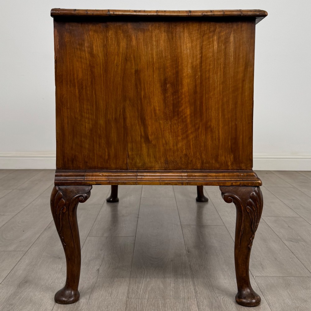 An 18th-century Queen Anne walnut chest of drawers featuring figured wood veneer, brass drop handles, and cabriole legs ending in pad feet. View VII