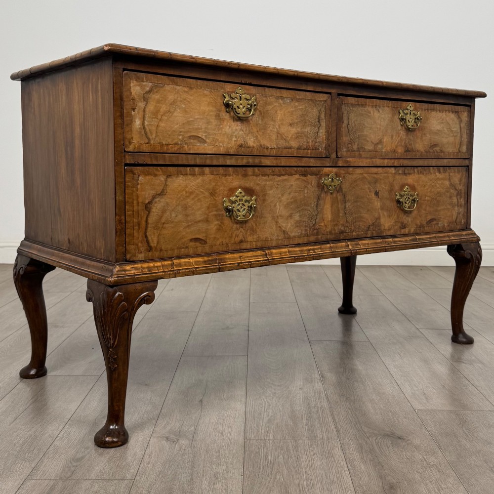 An 18th-century Queen Anne walnut chest of drawers featuring figured wood veneer, brass drop handles, and cabriole legs ending in pad feet. View VIII