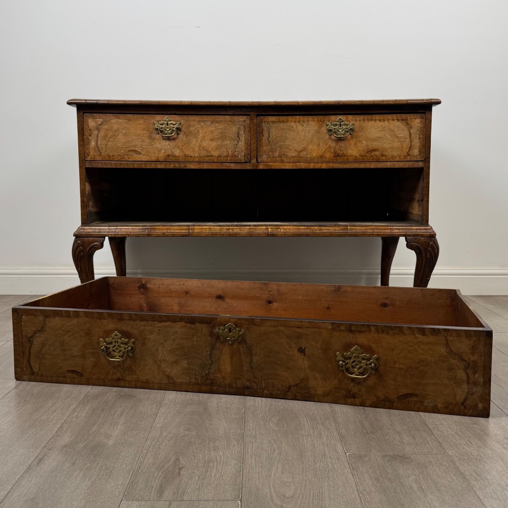 An 18th-century Queen Anne walnut chest of drawers featuring figured wood veneer, brass drop handles, and cabriole legs ending in pad feet. View X