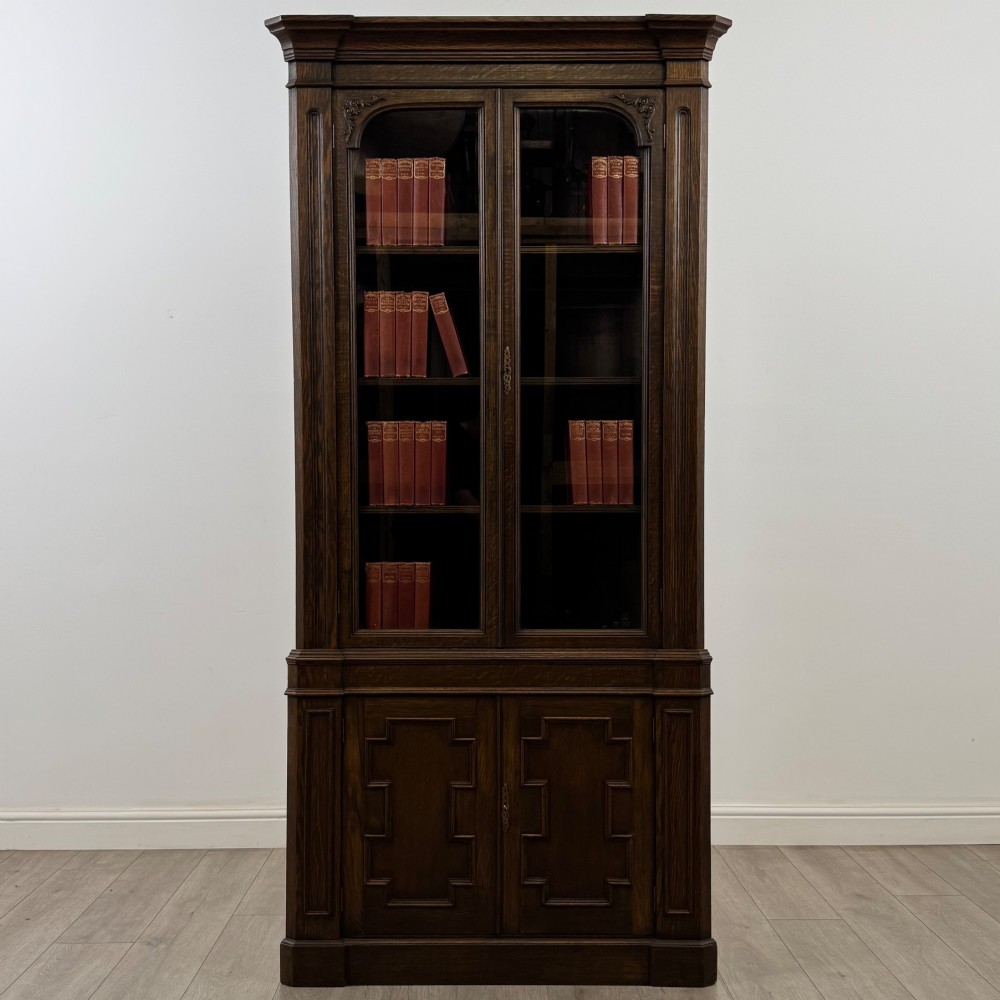 A tall dark oak Jacobean style corner cabinet featuring glazed display doors above lower cupboard doors with geometric fielded panelling.