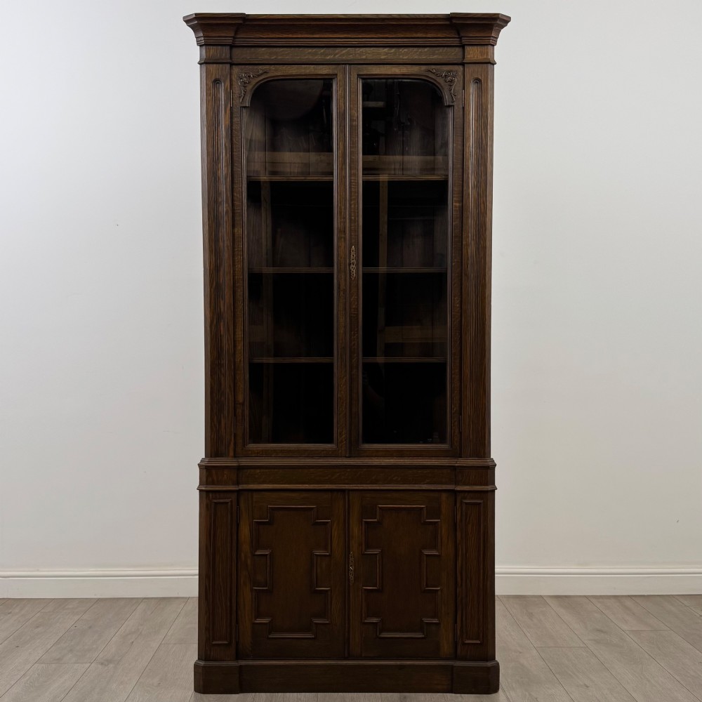 A tall dark oak Jacobean style corner cabinet featuring glazed display doors above lower cupboard doors with geometric fielded panelling. View II