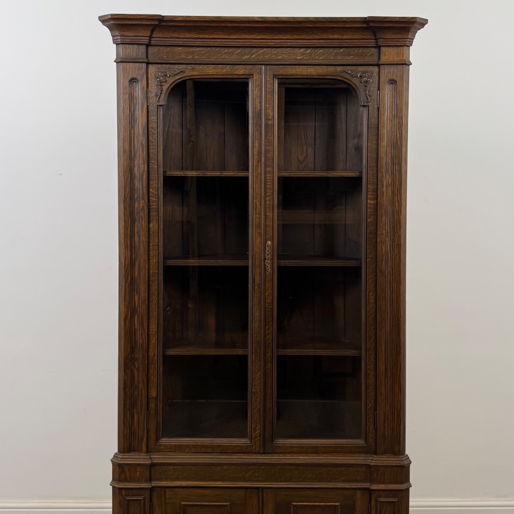 A tall dark oak Jacobean style corner cabinet featuring glazed display doors above lower cupboard doors with geometric fielded panelling. View V