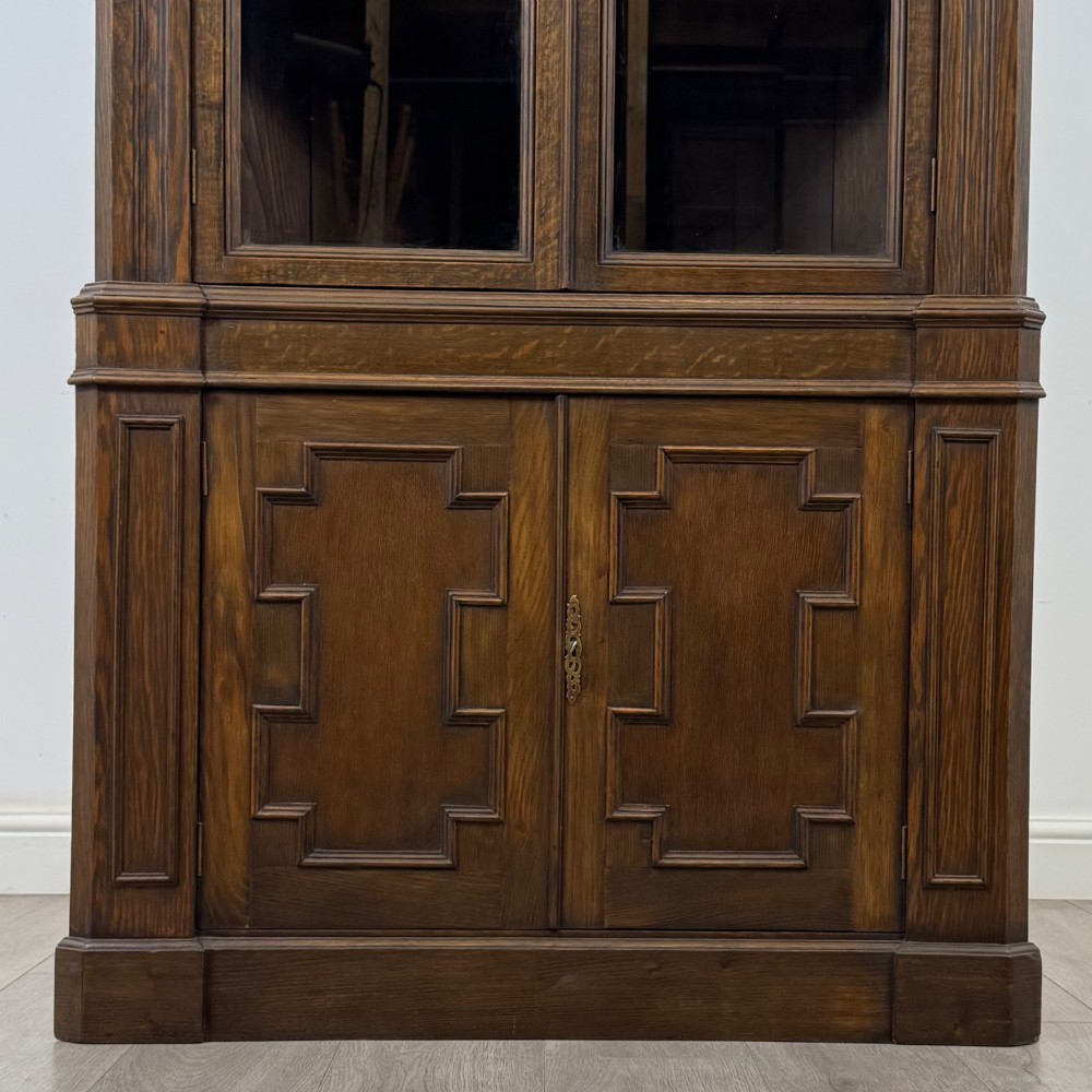 A tall dark oak Jacobean style corner cabinet featuring glazed display doors above lower cupboard doors with geometric fielded panelling. View VI